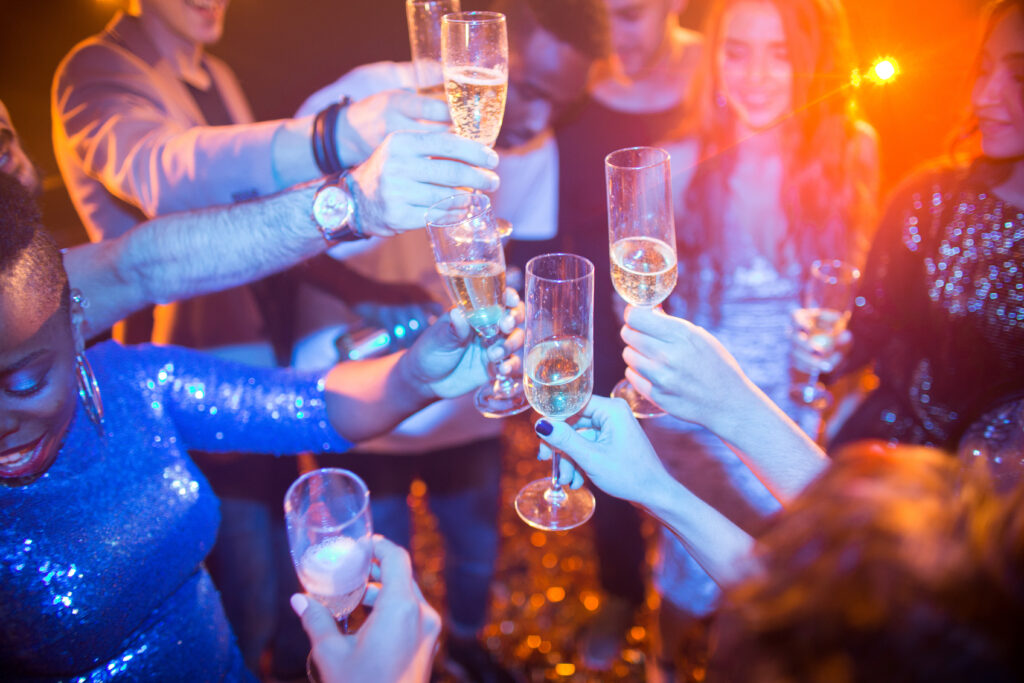 High angle view at multi-ethnic group of laughing young people enjoying dance party in nightclub and drinking champagne, focus on clinking glasses